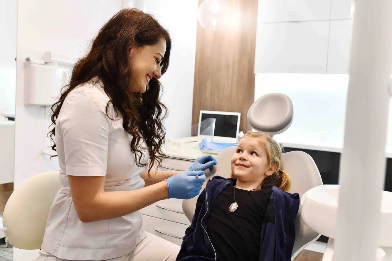 Dentystka rozmawia z uśmiechniętym dzieckiem w fotelu stomatologicznym